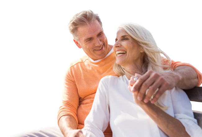 A mature, smiling couple sitting on a bench.